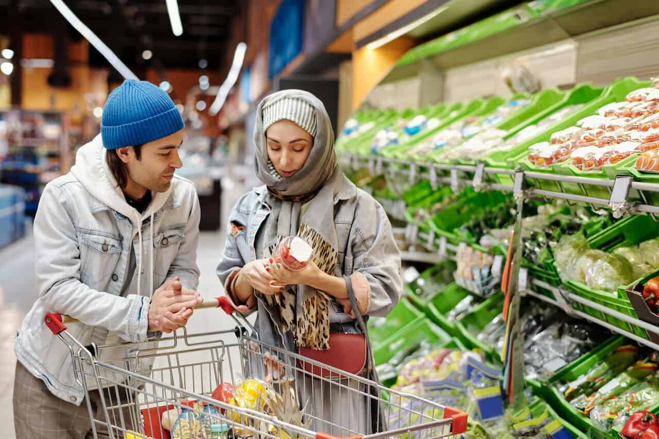 2 personen im supermarkt mit einkaufswagen vor gemüseregal